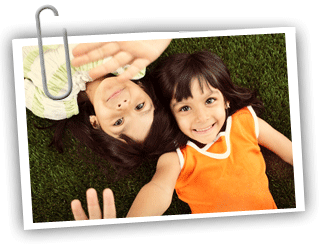 Two twin girls laying on their backs in the grass looking up at the camera and smiling