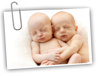 Two twin babies laying together with their arms wrapped together