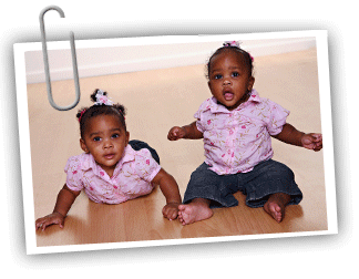 Two African American twin girls, one sitting and the other laying on the ground.