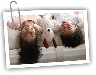Girl/boy African American twin pair laying upside down on a couch with a stuffed animal in between them
