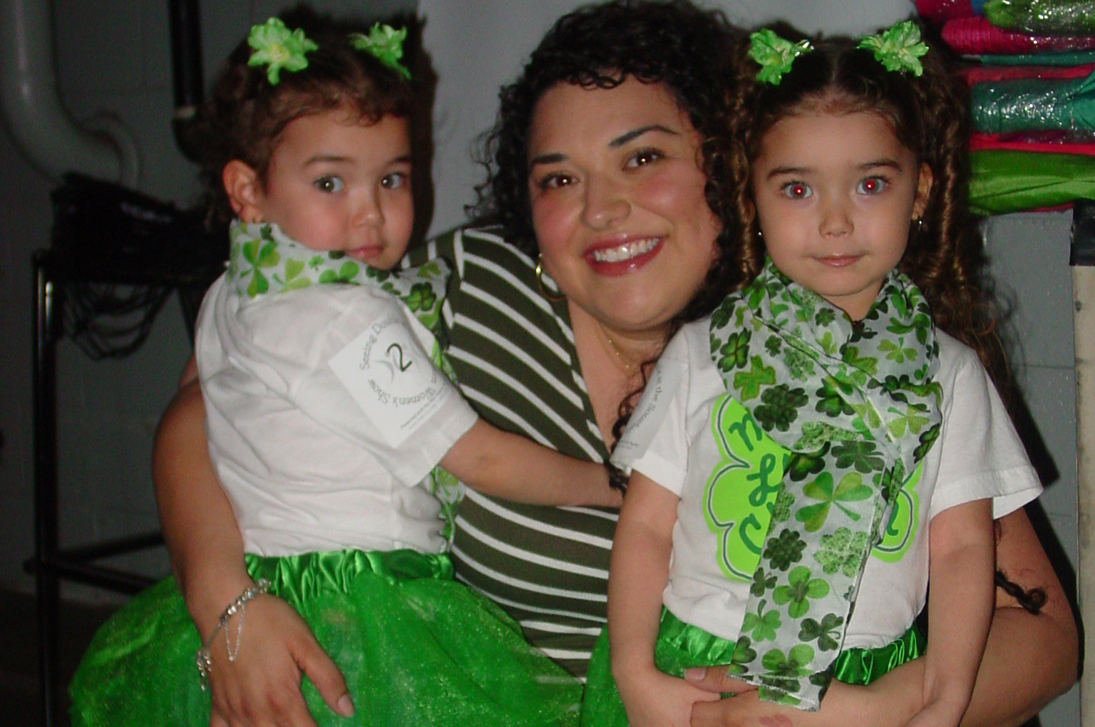 Mom holding her twin toddler girls, who are wearing green tutus