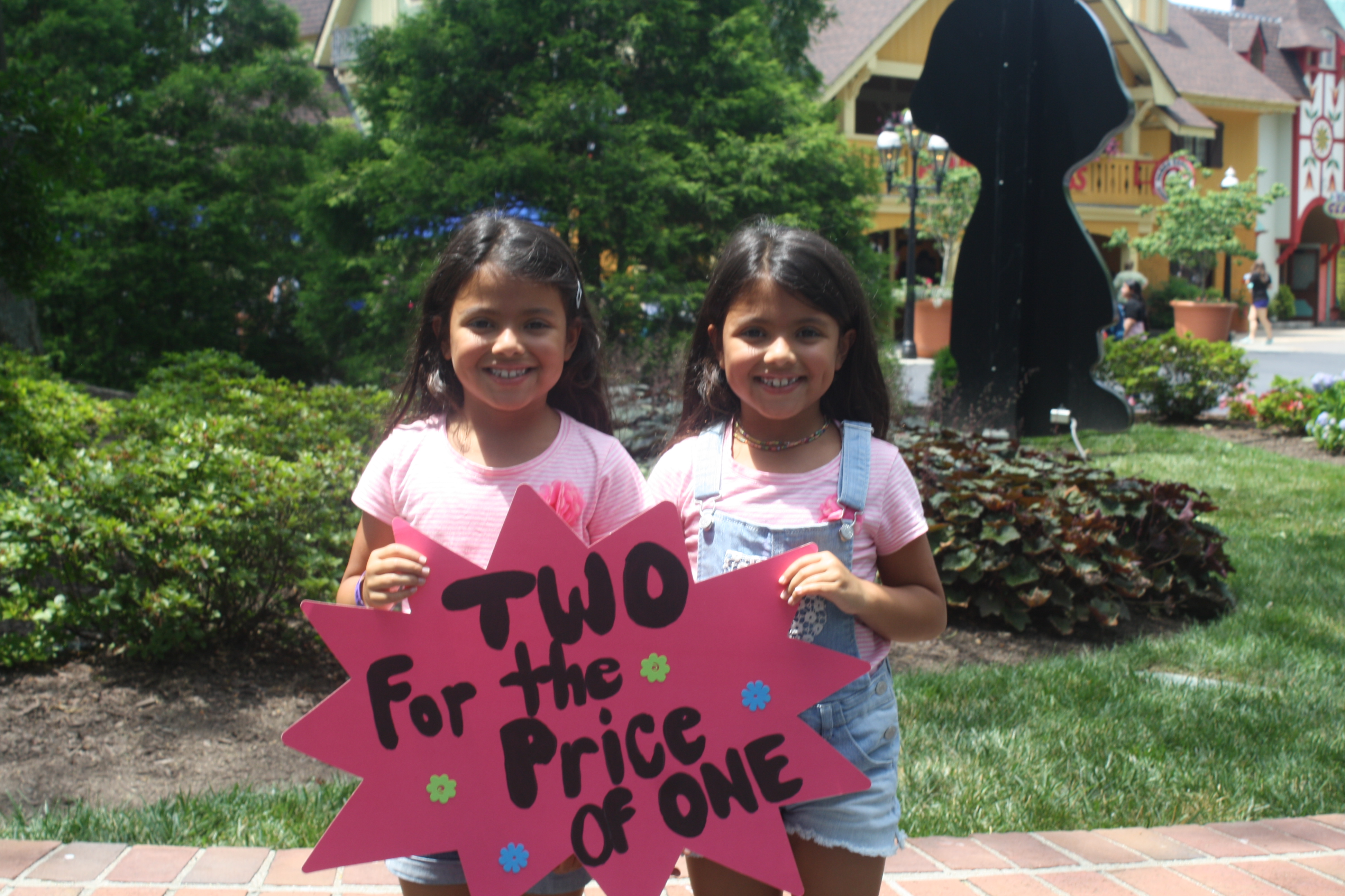Twin girls holding a sign that says Two for the Price of One