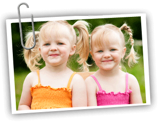 Two young twin girls with their hair in pigtails smiling at the camera