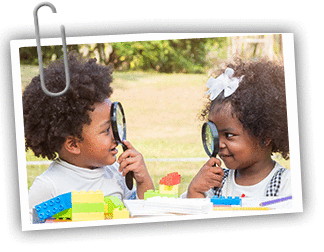 Twin African American baby boy and baby girl looking at each other while holding a magnifying glass